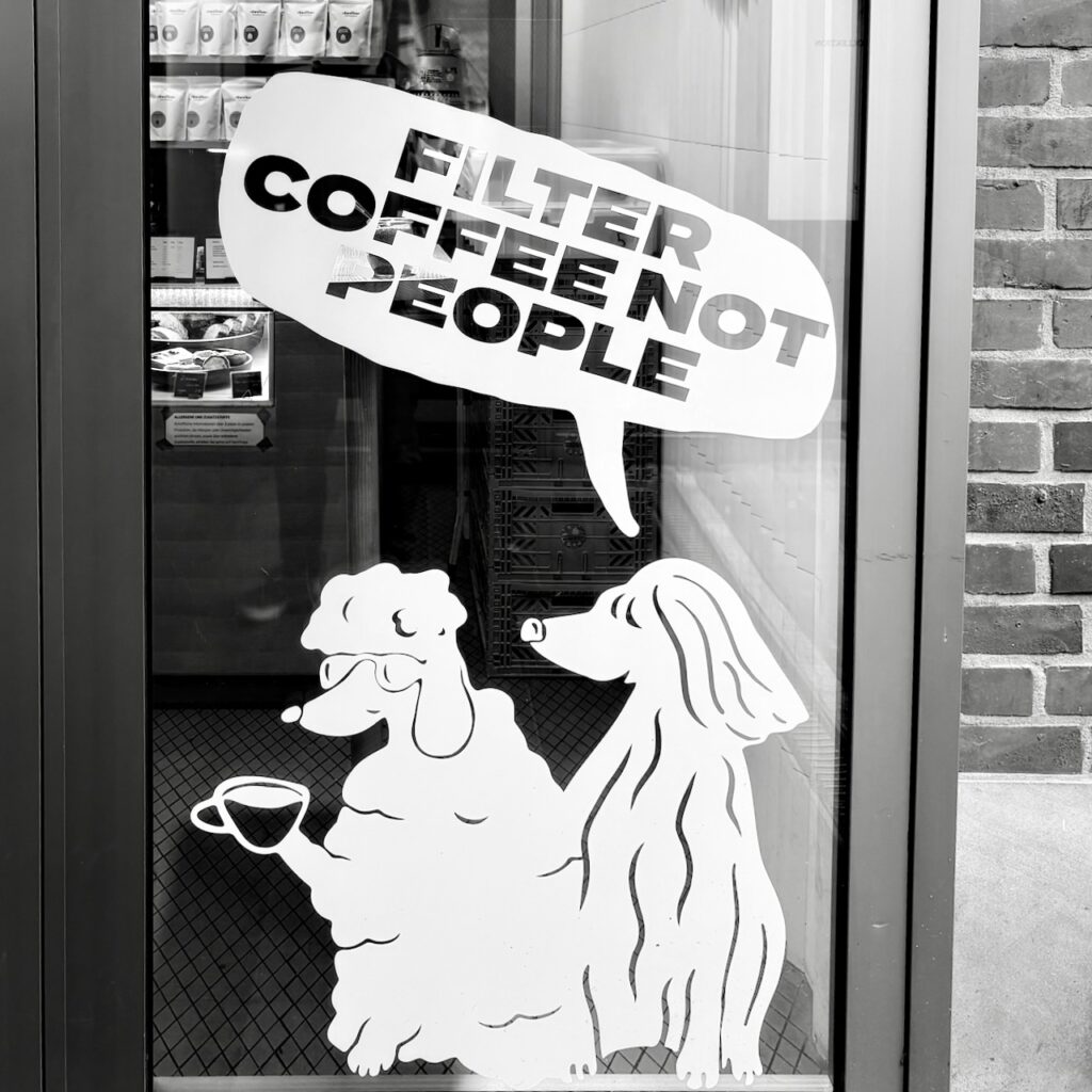 A photo of a coffee shop’s front window with the following text: ‘Filter coffee, not people’.